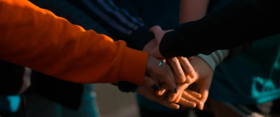 mehrere Menschen strecken ihre Hände zusammen und bilden damit ein Symbol der Gemeinschaft